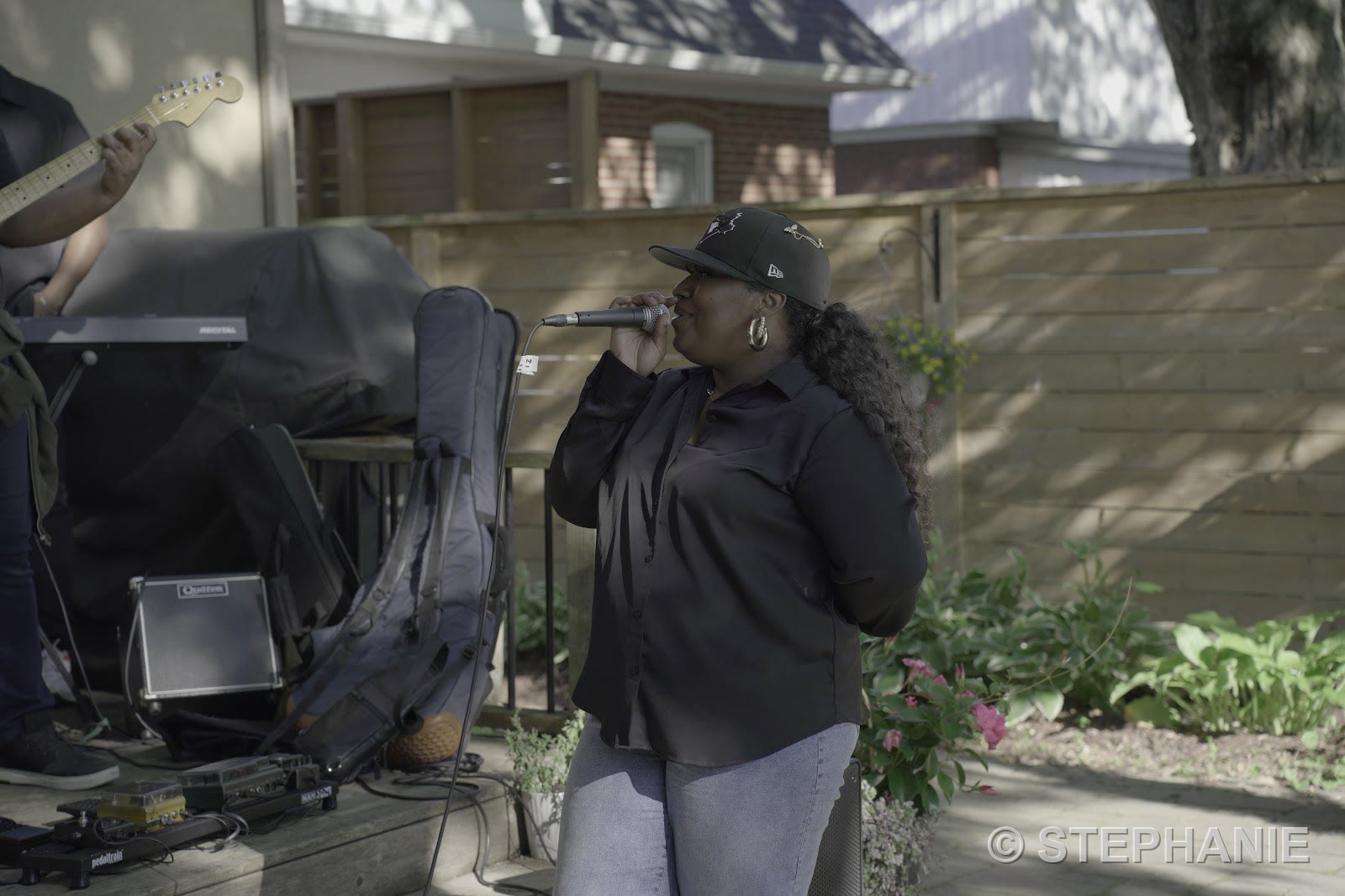 A vocalist in a black shirt and cap singing into a microphone beside the garden