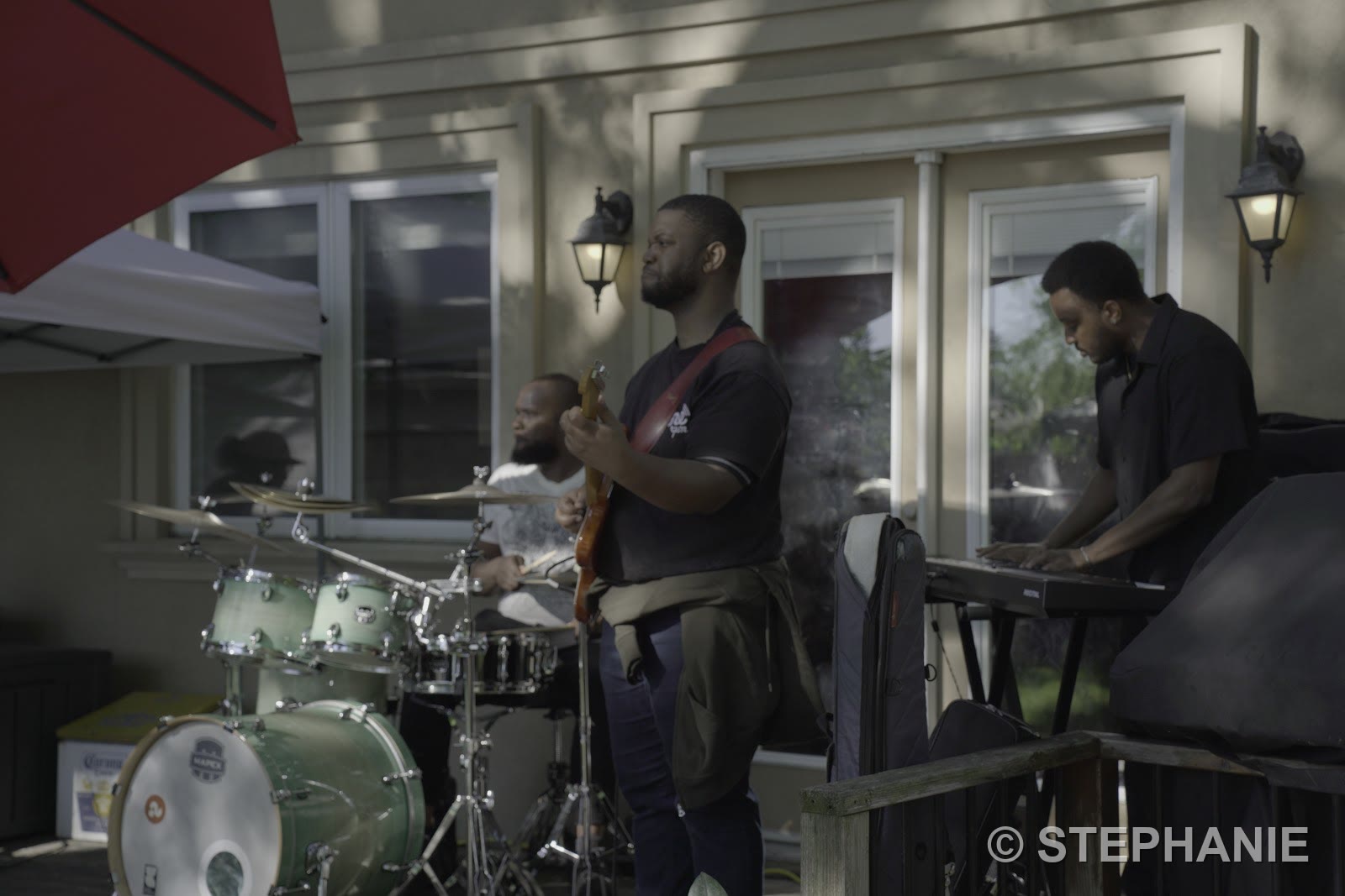The band settling in on the porch — drums, bass, and keys in the shade