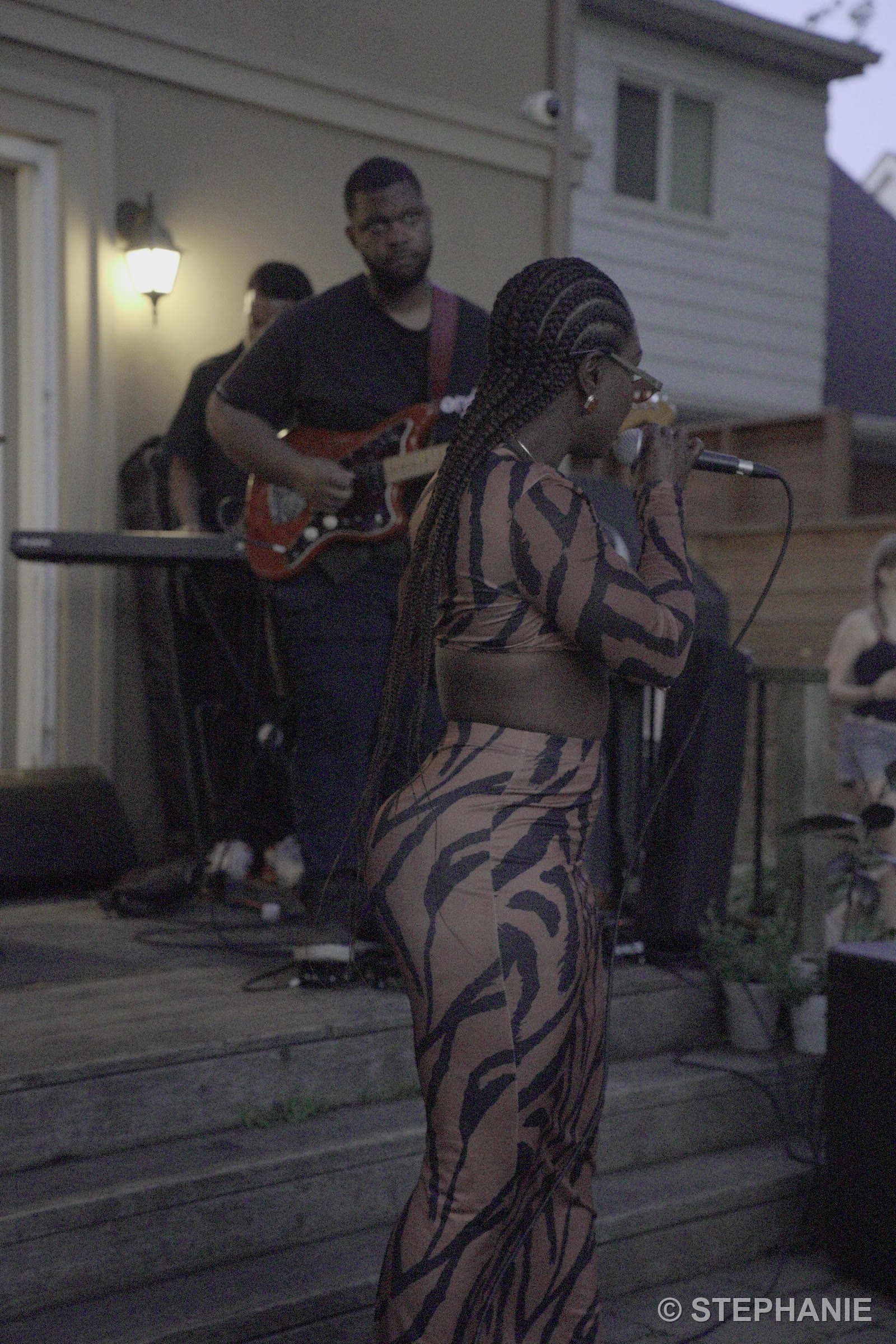 The singer from behind, braids down her back, facing the band at golden hour