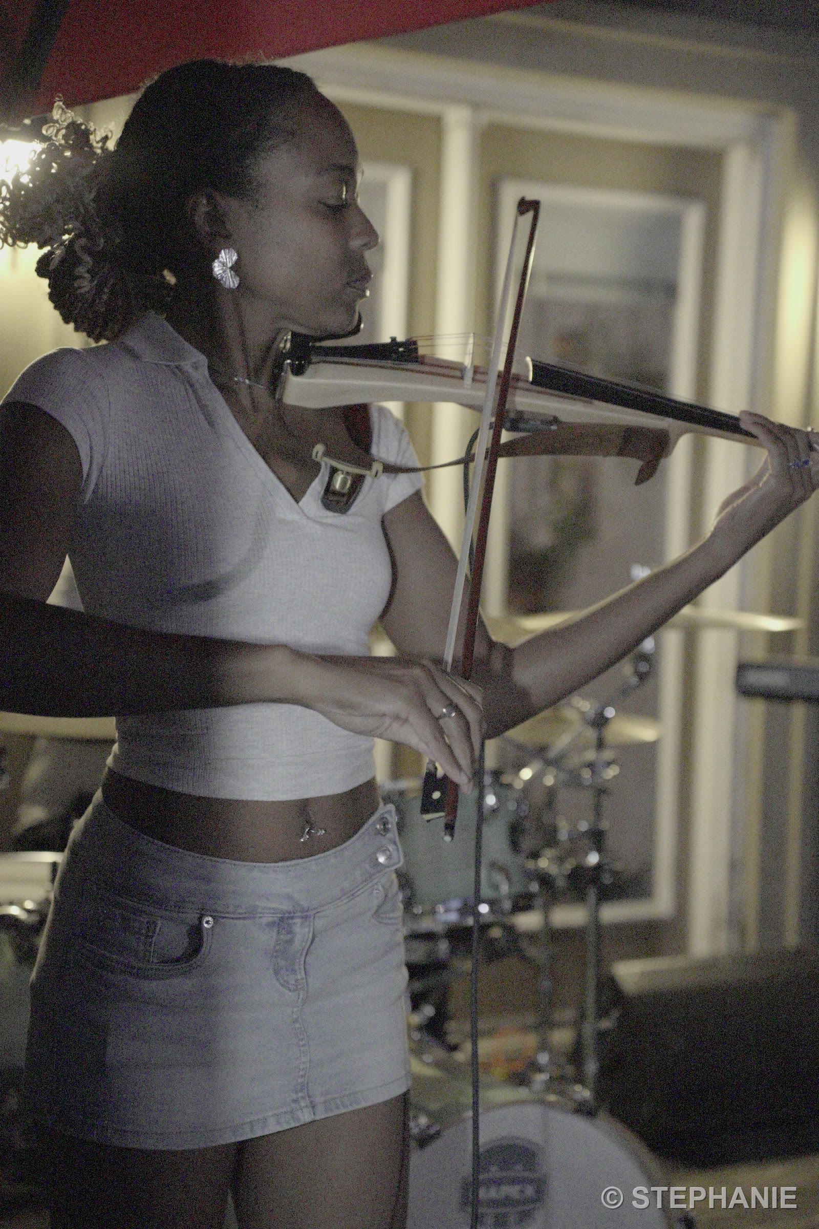 A violinist mid-bow in front of the drum kit, lit warm against the night