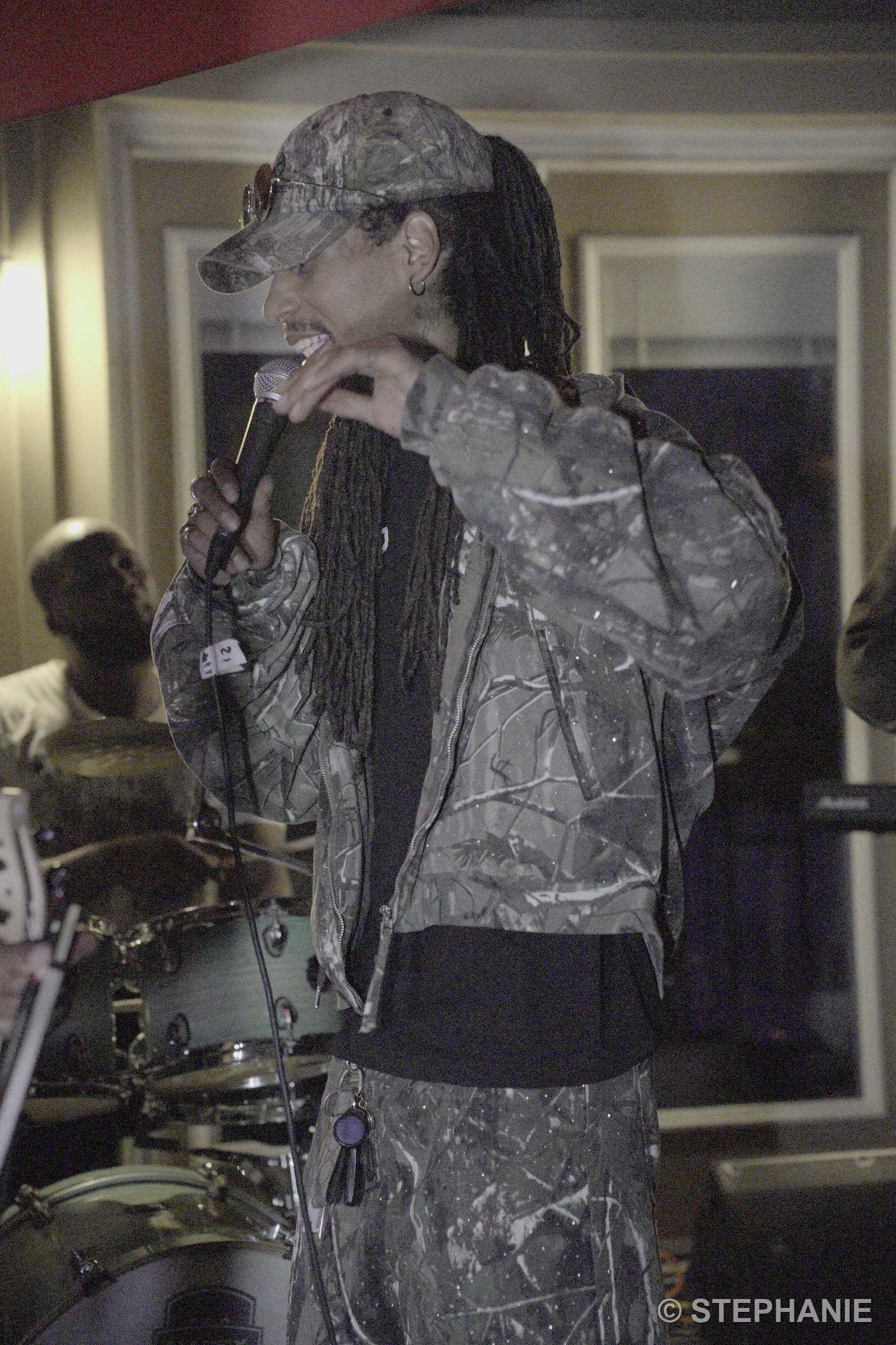 A vocalist in camo delivering a verse over the kit, deep in the night set